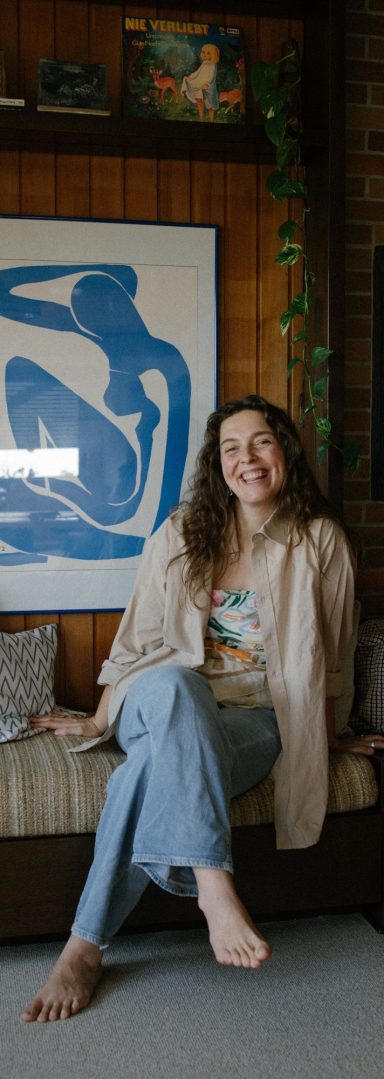 Lisa Schubert lächelt freundlich in die Kamera, vor einem blauen Bild im Hintergrund. Lisa Schubert sitzt vor einem blauen Bild und lächelt in die Kamera